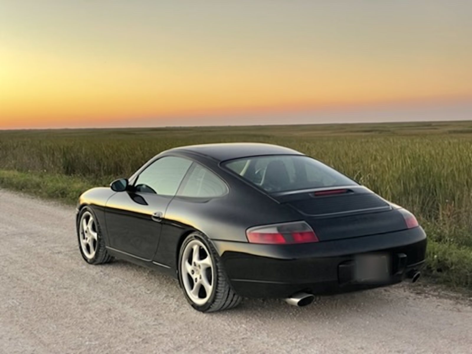 Black 996 Carrera coupe parked on a gravel road at sunset beside the Florida Everglades
